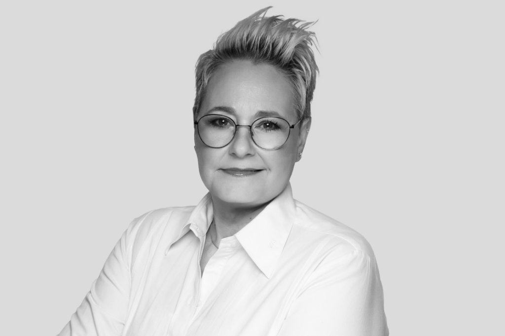 Schwarz-weiß Porträt einer Frau mit kurzer Frisur und runder Brille in weißer Bluse.