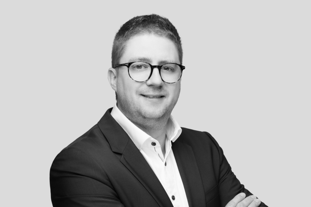 Schwarz-weiß Porträt eines Mannes mit Brille, hellem Hemd und freundlicher Ausstrahlung.