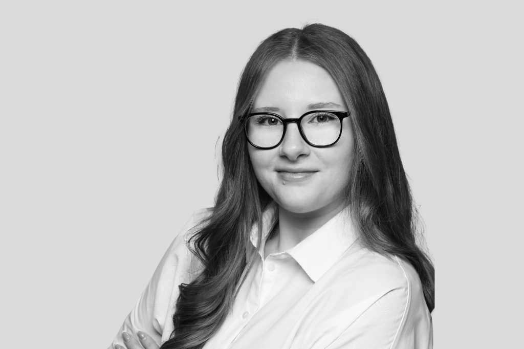 Schwarz-weiß Porträt einer jungen Frau mit Brille, langen Haaren und weißer Bluse.